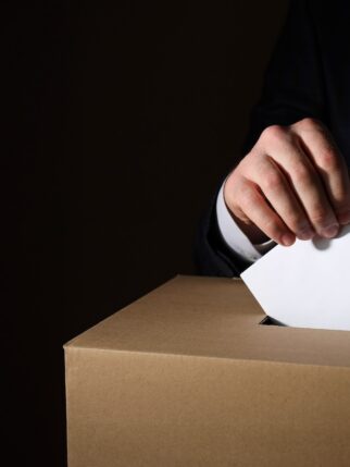 Paper box and hand with voting paper on dark background, space for text